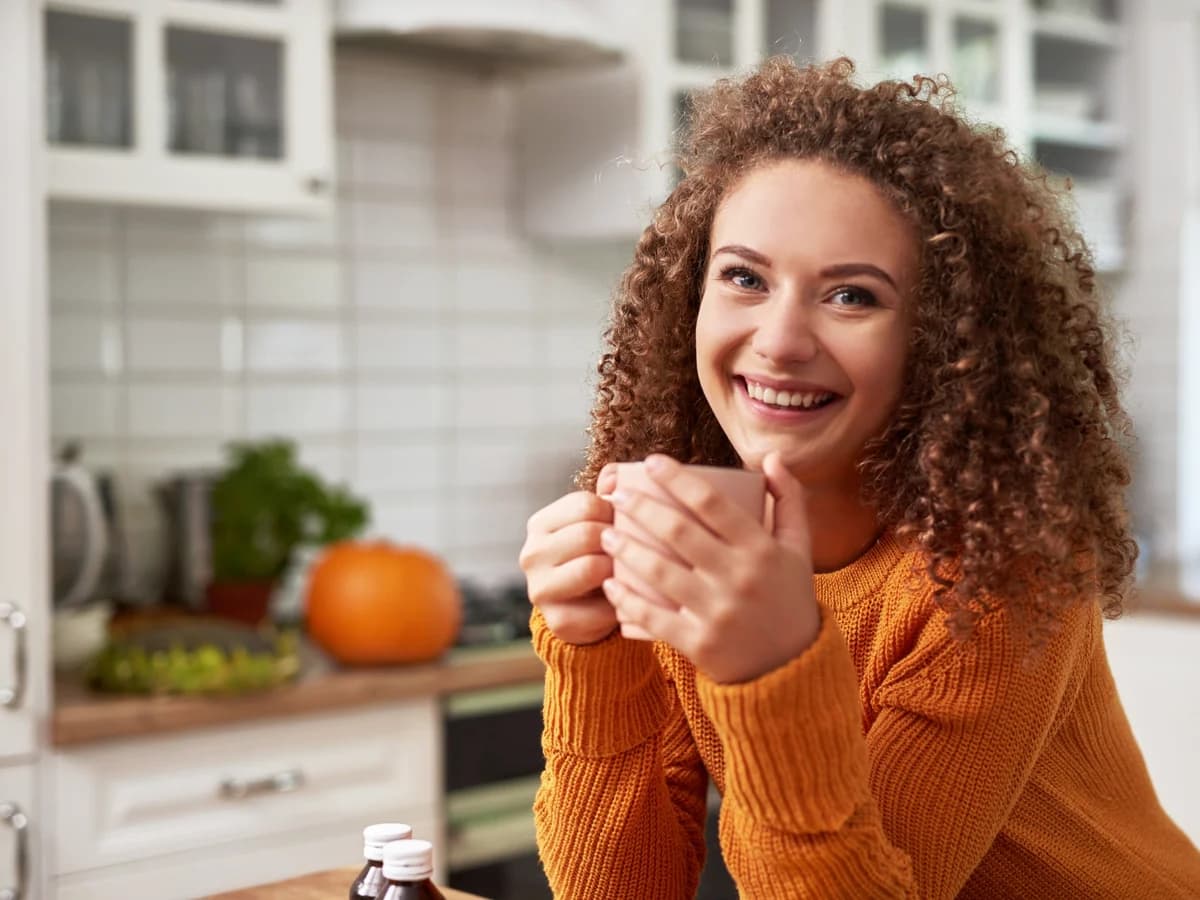 A woman holding a cup of tea in a bright kitchen.